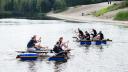 Twee vlotten met op elk 4 personen met peddels die tegen elkaar racen